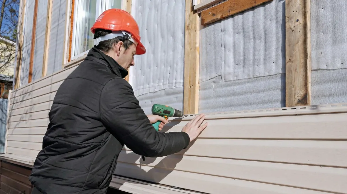 Siding replacement professional using a power drill to install new tan vinyl siding on a home exterior in Albuquerque, NM